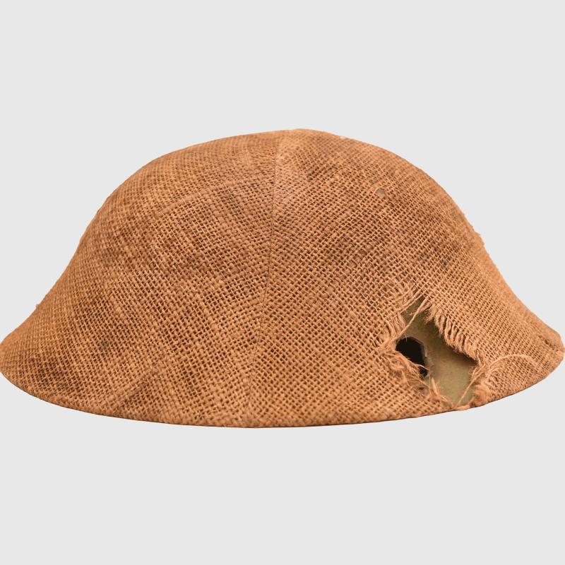 BRITISH WWI VERY FIRST PATTERN BRODIE HELMET IN GREEN WITH BATTLE DAMAGE AND FIELD COVER.